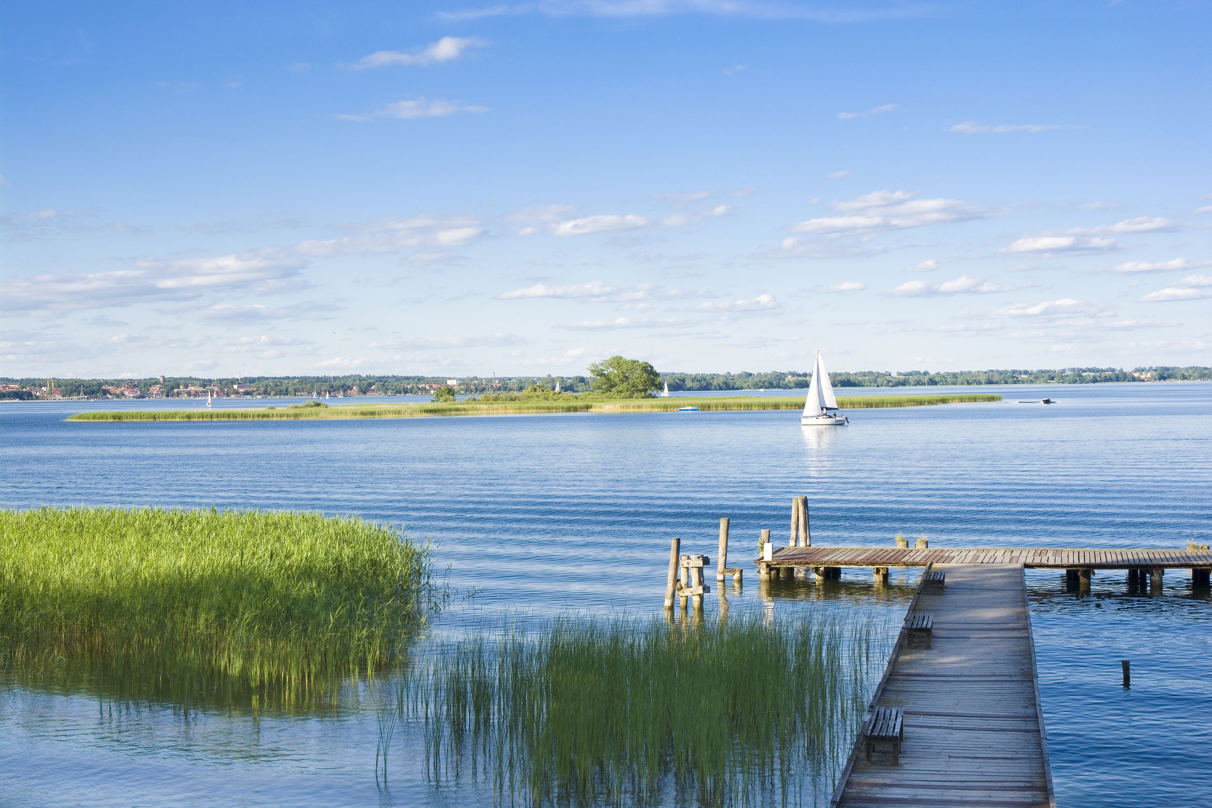 Empty wooden jetty on the lake shore with island and yachts in the bac