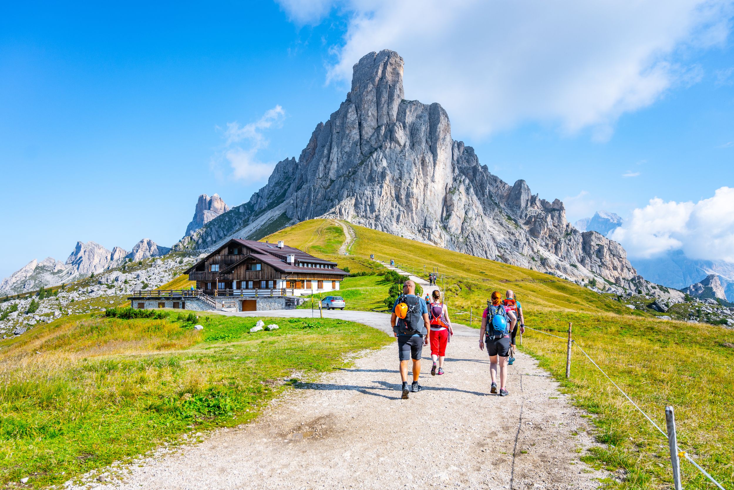 Group of hikers walks towards mountains on sunny summer day. Giau Pass