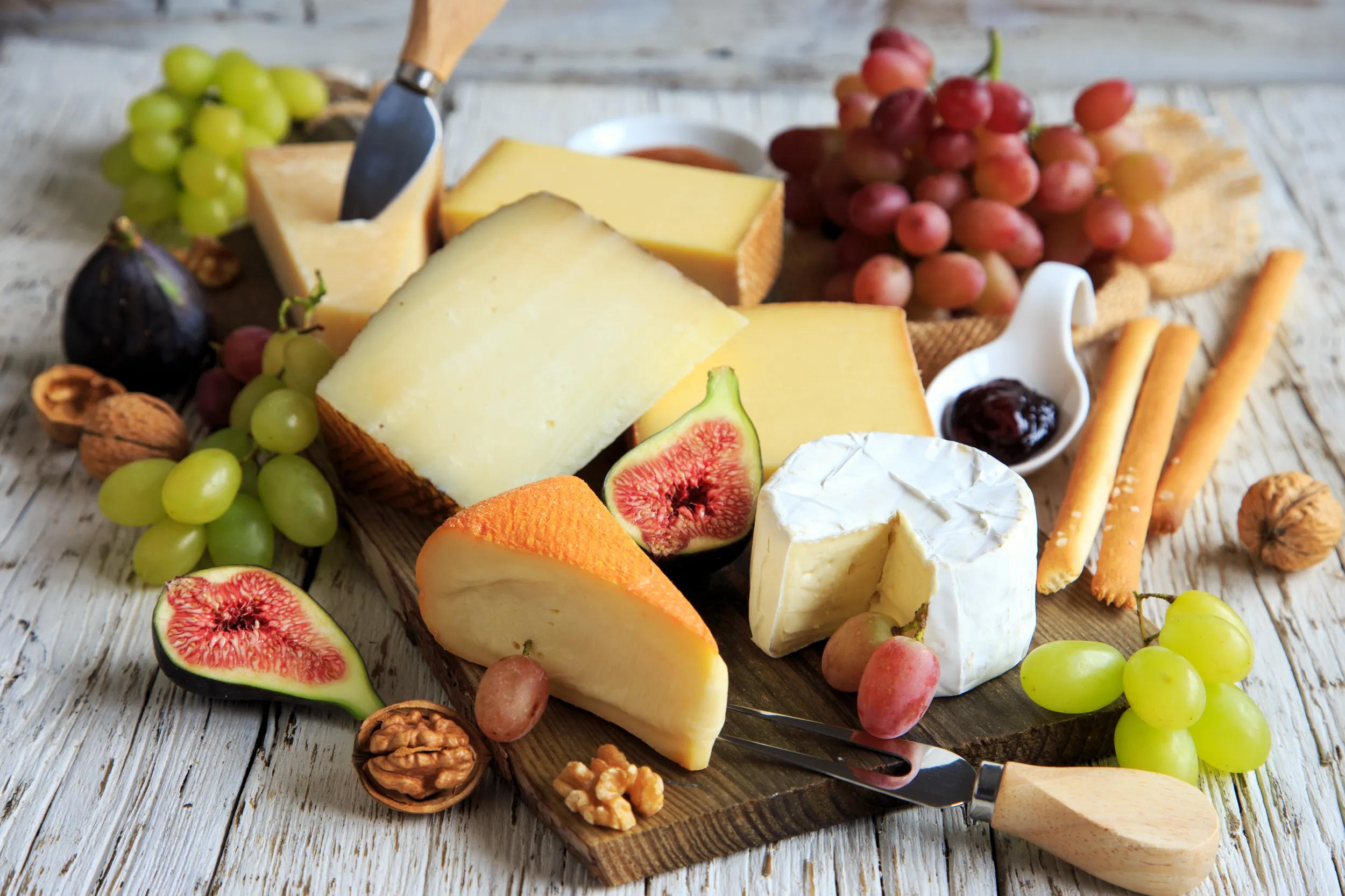 Holzbrett mit Südtiroler Ziegenkäse, garniert mit Walnüssen und frischem Thymian, dazu halbierte Feigen, dunkle Trauben und ein Glas Honig mit Holzlöffel.