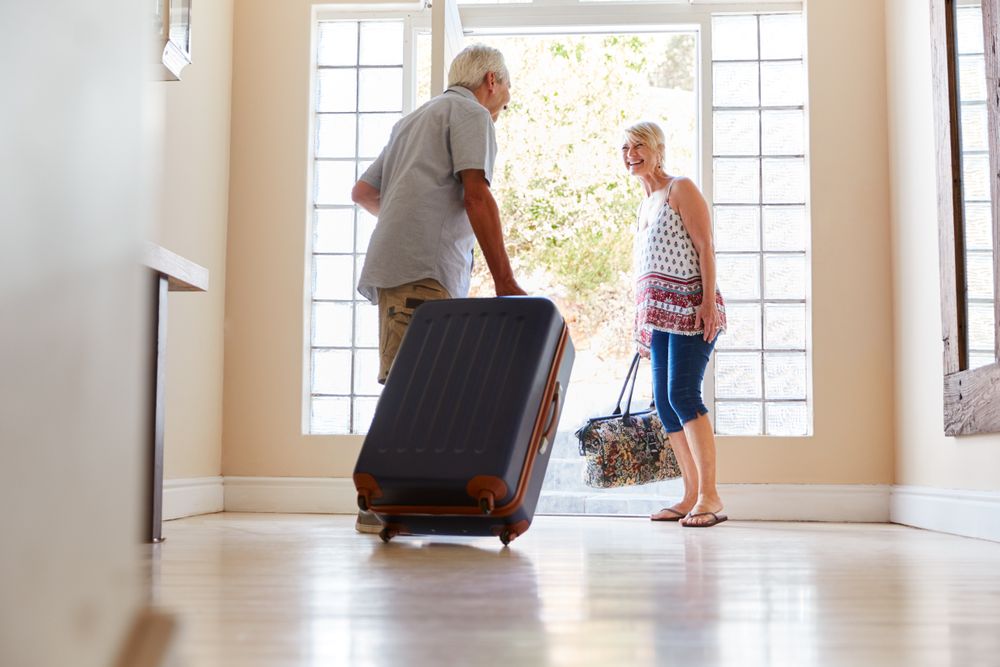 glückliches Rentnerpaar verlässt mit Koffern das Haus