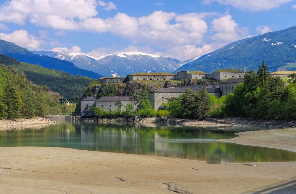 Festung Franzensfeste in Südtirol mit Blick auf den angrenzenden Stausee, umgeben von bewaldeten Hängen und verschneiten Berggipfeln im Hintergrund